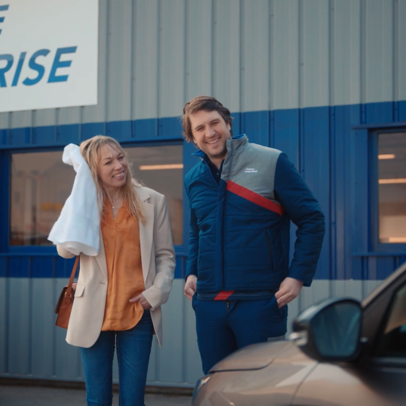 Deux personnes souriantes se tiennent devant un établissement appelé 