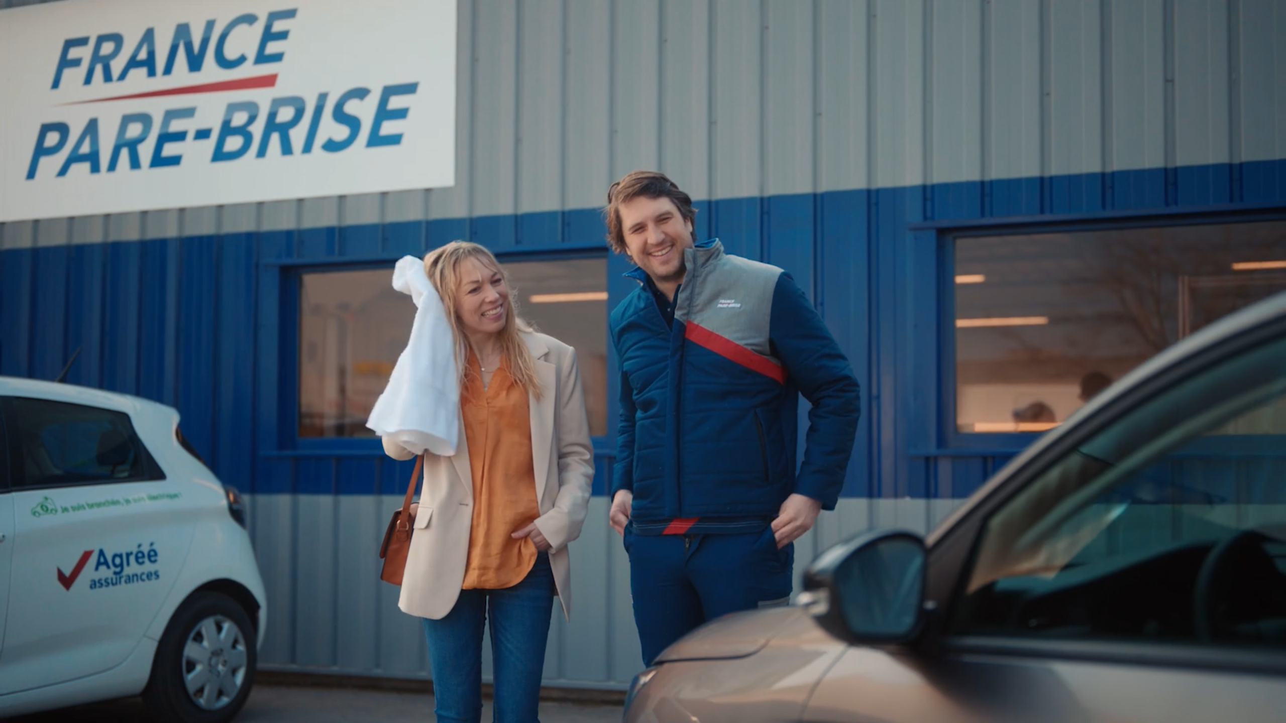 Deux personnes souriantes se tiennent devant un établissement appelé "France Pare-Brise".