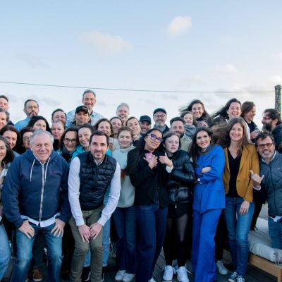 Un grand groupe de personnes souriantes pose ensemble à l'extérieur sous un ciel bleu, créant une atmosphère conviviale.