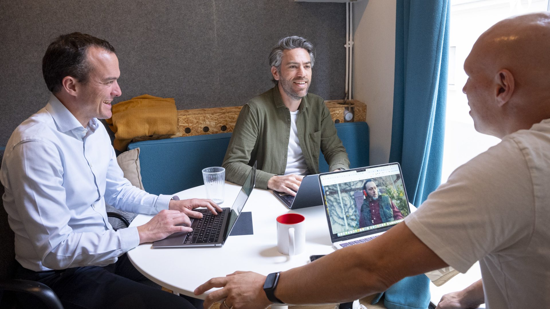 Trois hommes sont assis autour d'une table, travaillant sur des ordinateurs portables, dans un environnement de bureau contemporain.