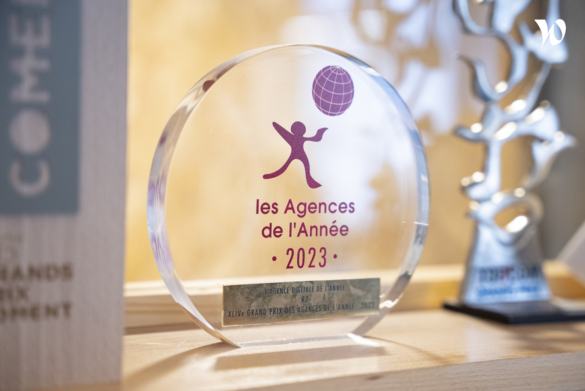 Un prix en verre gravé indiquant "les Agences de l’Année 2023" avec une mention spéciale pour "l’Agence Digitale de l’Année" à côté d'une autre statuette.