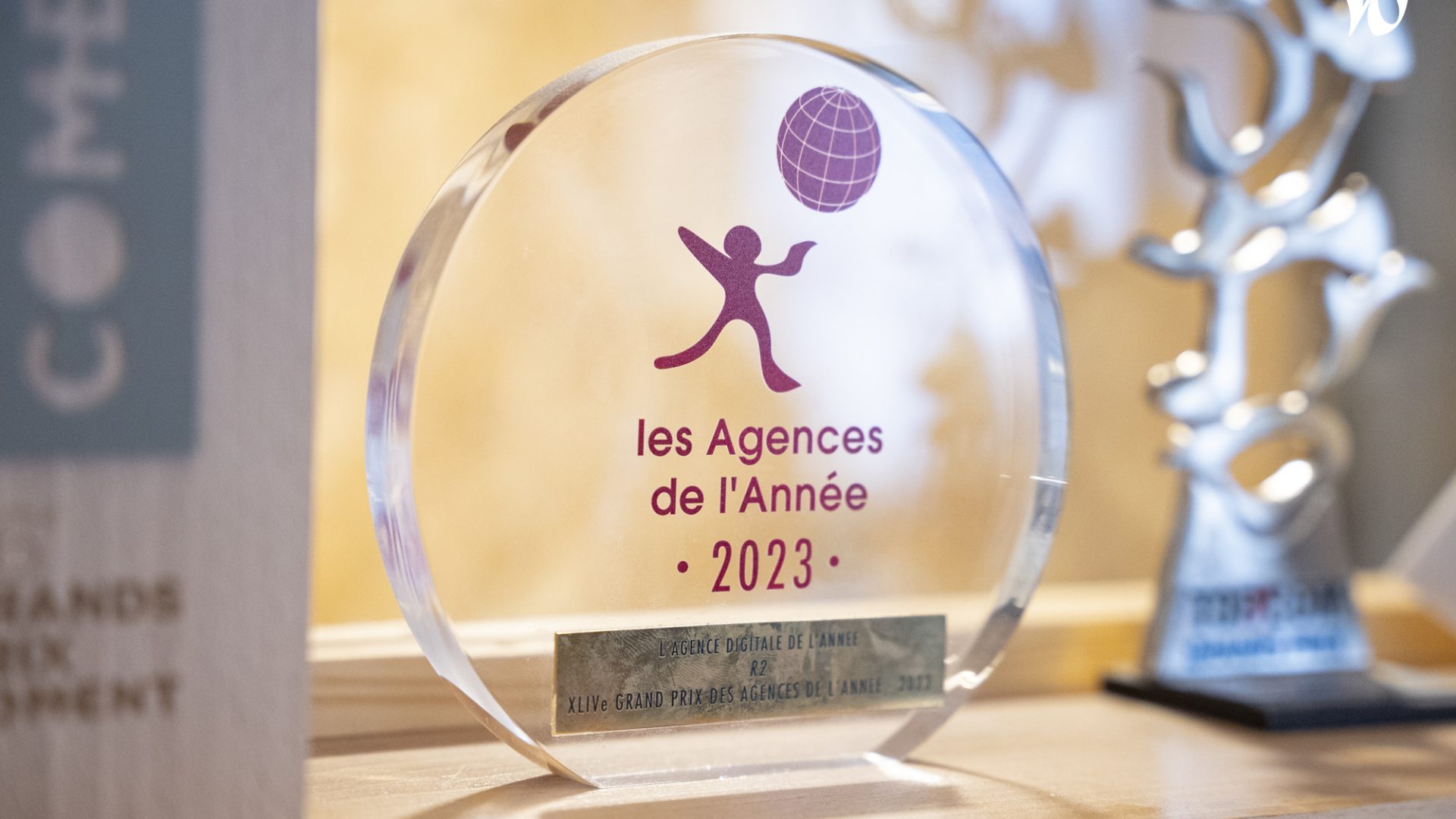 L'image présente un trophée en acrylique transparent pour "les Agences de l’Année 2023", indiquant une récompense pour l'agence digitale de l'année.