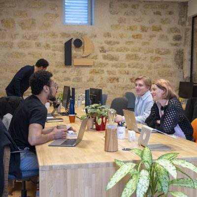 Des personnes échangeant et travaillant ensemble dans un espace de bureau moderne et décontracté avec des plantes et des ordinateurs.