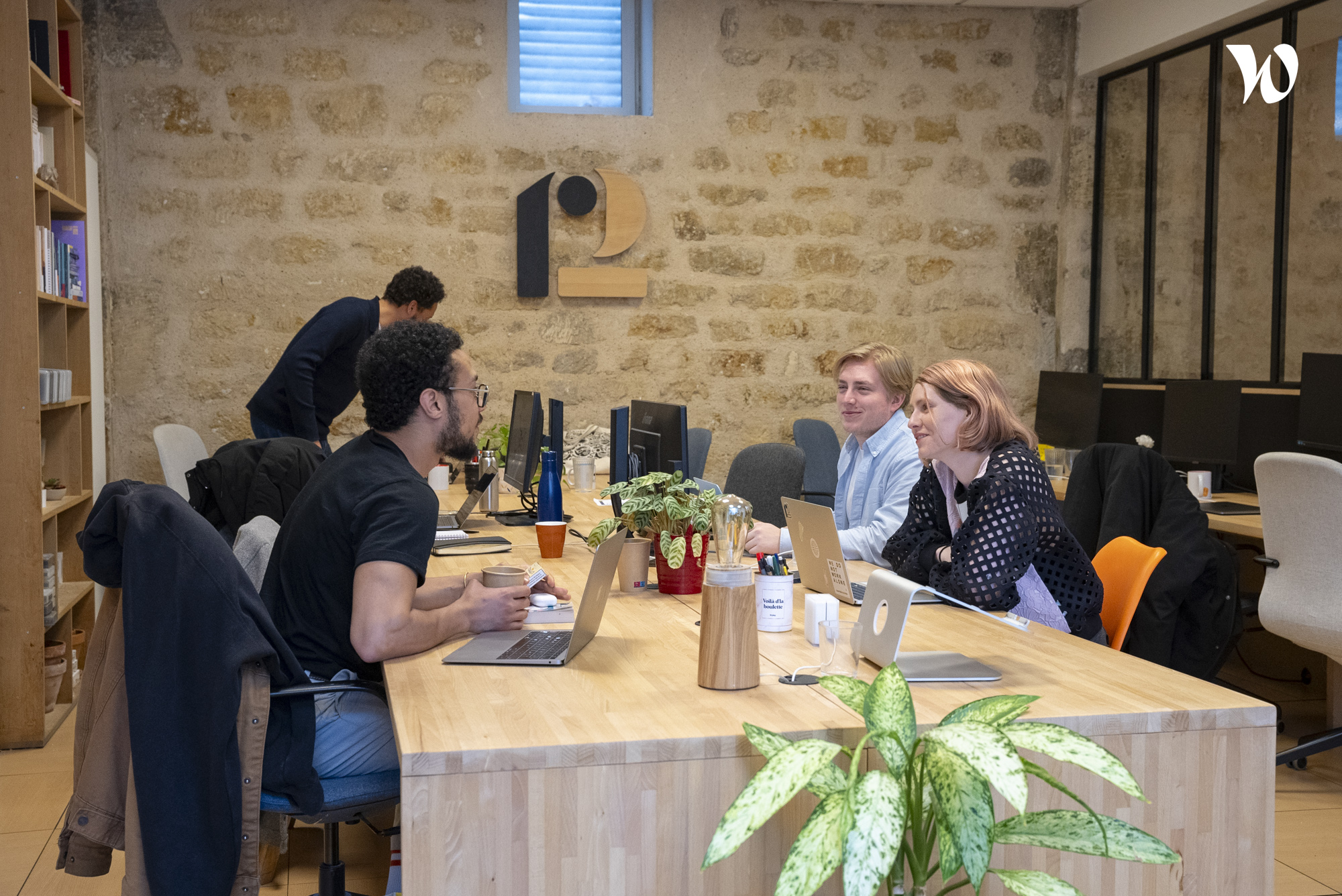 Des personnes échangeant et travaillant ensemble dans un espace de bureau moderne et décontracté avec des plantes et des ordinateurs.
